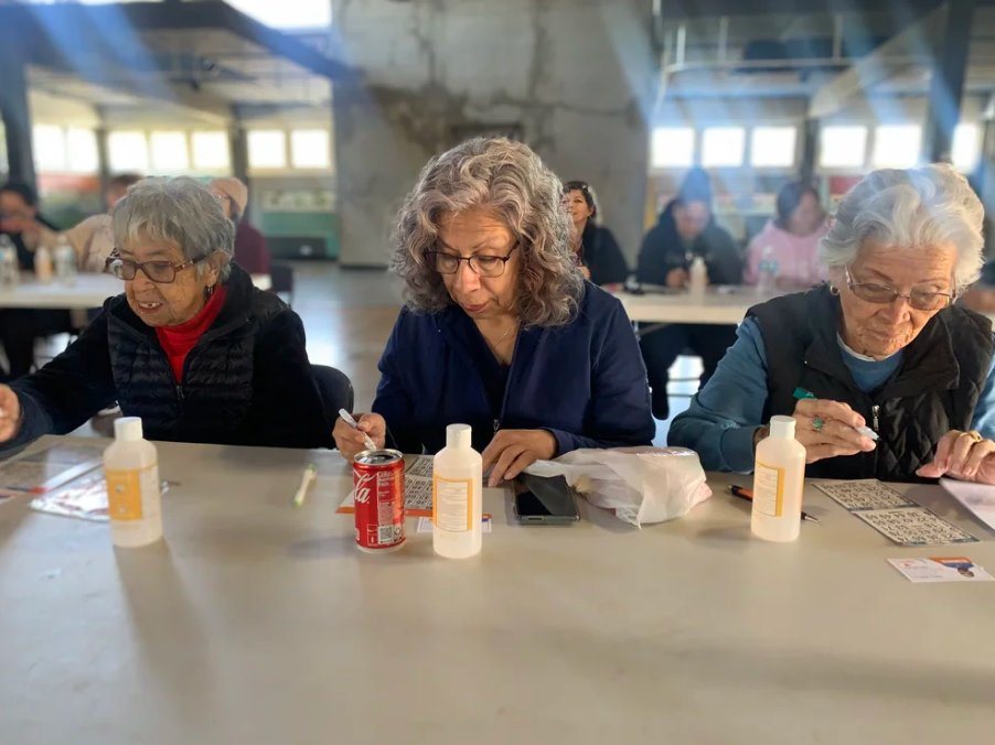 Three older women concentrating on their lotería cards at a long table
