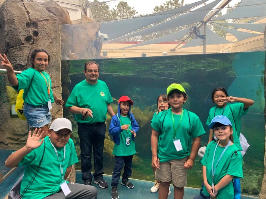 Kids in matching green camp shirts posing in front of an aquarium tank