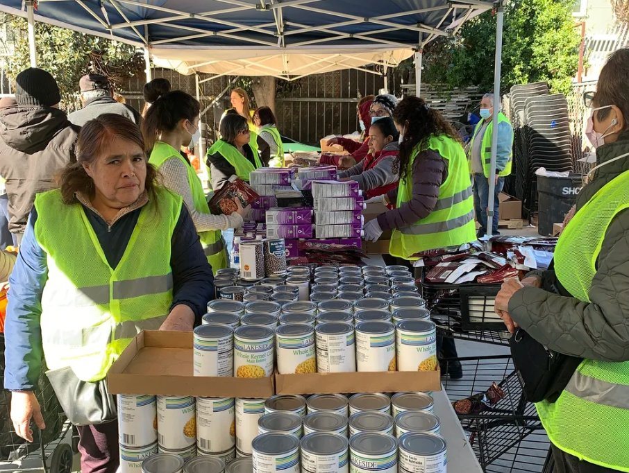 Volunteers in safety vests organizing canned goods at an outdoor food distribution