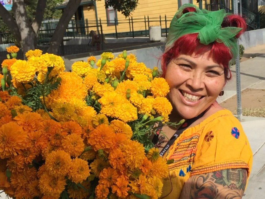 Smiling woman carrying a huge armful of orange marigolds