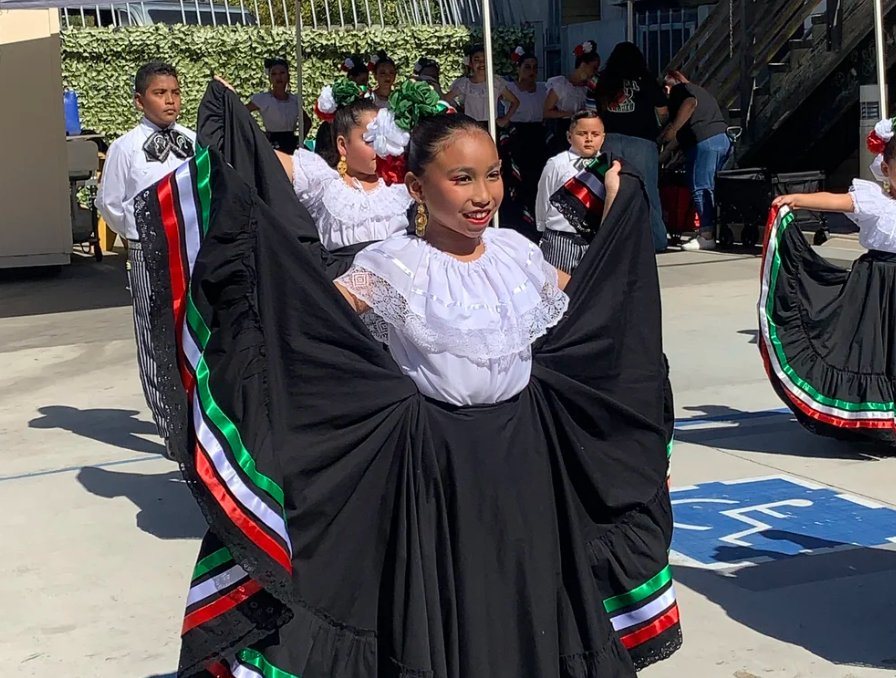 Young folklórico dancer in a black skirt with green, white, and red ribbons mid-performance