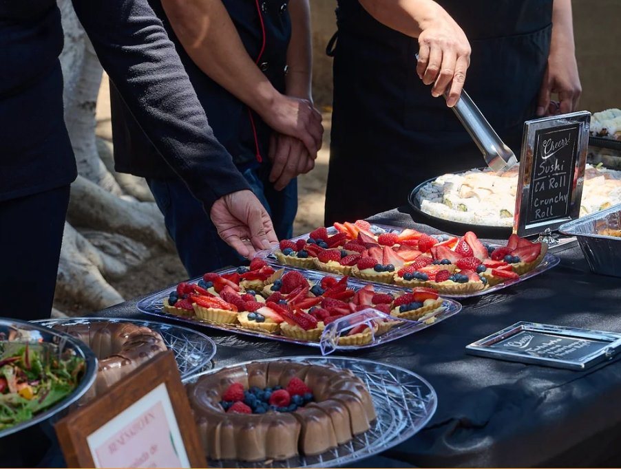 Trays of fruit tarts and desserts being served at an outdoor event table